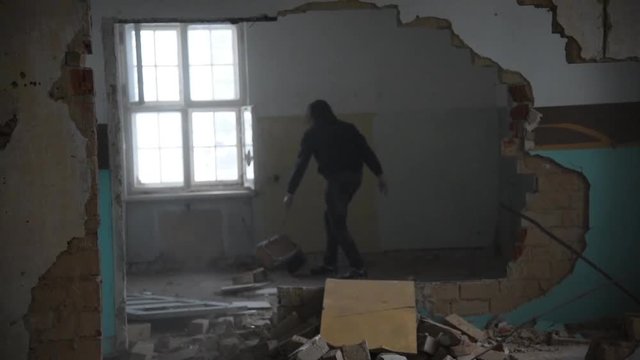 Depressed and mad man throws a chair through a room in an old abandoned house