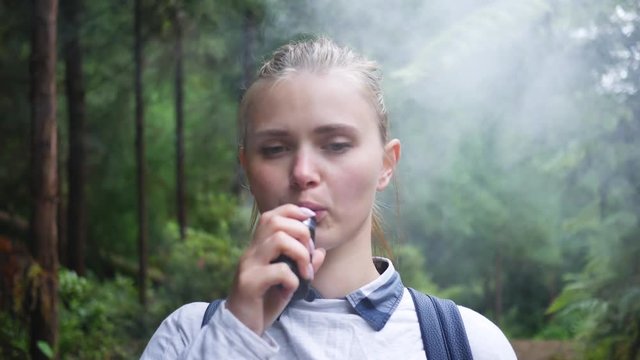 girl uses electronic cigarettes in a beautiful green forest