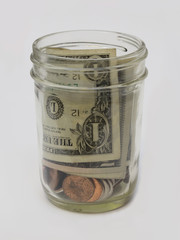 A small tip jar, filled with U.S. dollars and cents, is shown isolated, set against a whilte background.
