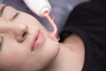 Receiving electric darsonval facial massage procedure at beauty salon