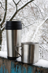 Iron mugs of hot drink on a snow covered terrace.