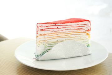 Rainbow crape cake on white plate on wooden table..