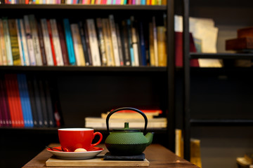 Tea time in book shop. Tea pot and cup on the wooden table.