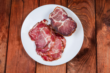 Partly sliced dried pork neck on white dish, top view