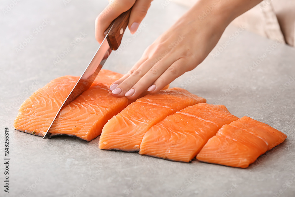 Wall mural woman cutting fillet of fresh salmon at table