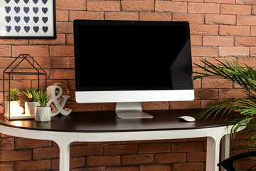 Modern computer on table near brick wall