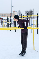 Fit man working with own body weight workout triceps and biceps on horizontal dips bars on snow in winter