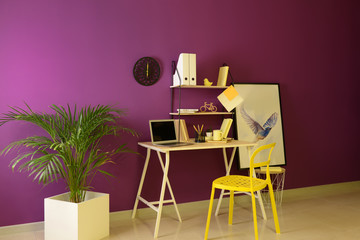 Stylish workplace with modern laptop near color wall