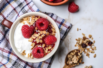 Bowl with tasty yogurt, oatmeal and raspberry on light background