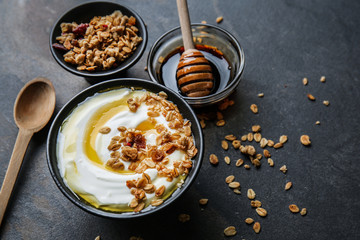 Bowl with tasty yogurt, honey and oatmeal on dark background