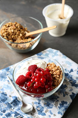 Glass bowl of tasty yogurt with jam, berries and oatmeal on table