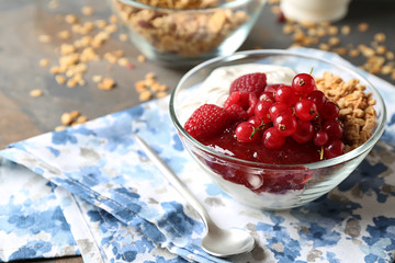 Glass bowl of tasty yogurt with jam, berries and oatmeal on table