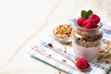 Glass jar of tasty yogurt with raspberry and oatmeal on table
