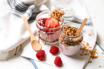 Glass jars of tasty yogurt with jam, strawberry, oatmeal and candied nuts on table