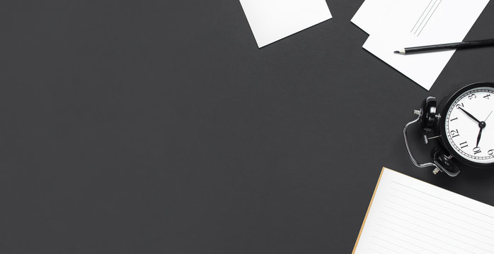 Flat lay cup of black coffee black alarm clock open notebook pencil white cards on gray dark background top view copy space. Minimalistic food concept morning breakfast time to work hot drink coffee