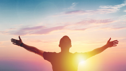 Young man standing outstretched at sunset. Victory