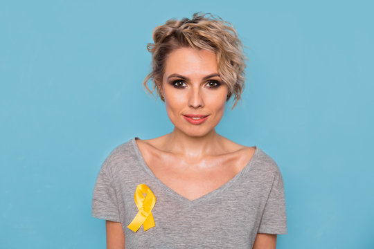 Young female holding yellow gold ribbon awareness symbol for endometriosis, suicide prevention, sarcoma bone cancer, bladder cancer, liver cancer and childhood cancer concept. Health care. Close up.