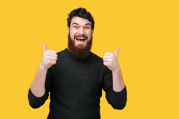 Happy bearded man showing thumbs up over yellow background