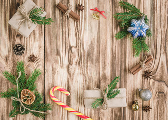 Christmas composition of fir branches with Christmas sticks, cones, cinnamon sticks, badian, balls, gift boxes on wooden table with copy space.