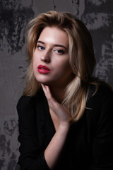 Lovely blonde woman with perfect makeup wearing black jacket posing at studio with shadows