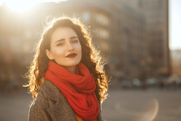 Spring portrait of pleased young model with wavy hair wearing oversize coat and red scarf. Space for text