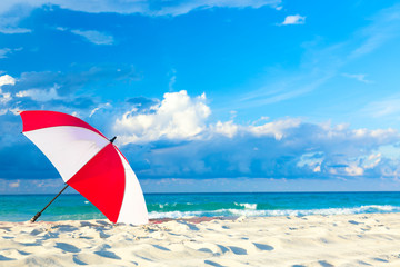 Colourful red and white umbrella on the ocean beach with beautiful blue sky and clouds. Relaxation, vacation idyllic background.