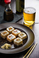 Sushi on a wooden plate with a glass of beer, soy sauce and natural wooden chopsticks on a light wooden table.