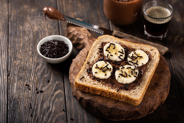 Delicious open sandwich with chocolate and banana on old wooden board and dark table. Food background with copy space.