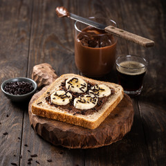 Delicious open sandwich with chocolate and banana on old wooden board and dark table. Breakfast background with copy space.