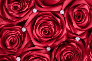 Festive hand made roses from satin ribbon and white beads background.