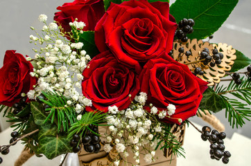 Bouquet of red roses, surrounded by sprigs of white gypsophila,berries, and conifer twigs in a small wooden box





