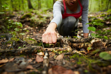 Hand of young sportswoman holding by dirty snag on the ground while moving forwards in the forest during training