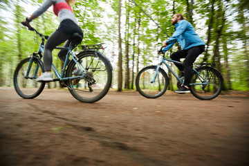 Young active couple riding their bicycles along road surrounded by group of blurry green trees