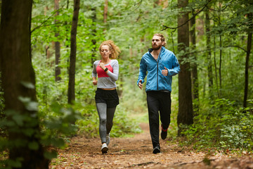 Young sporty couple running down forest path or in park in the morning between green trees