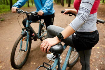 Fototapeta na wymiar Young sportswoman with smartwatch and bicycle and her boyfriend having short break during cycle chill