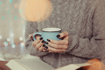 Beautiful girl holds mug with drink and reads book