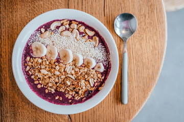 Beautiful blueberry banana smoothie bowl with a spoon on wooden table. Healthy breakfast concept.