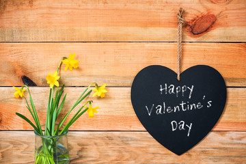 Happy valentine's day written on a chalkboard in the shape of a  heart, daffodils and wooden planks background
