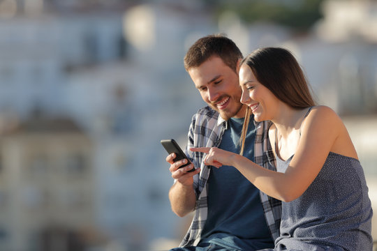 Happy Couple Browsing Cell Phone Content In A Town