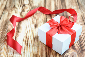 Gift box with red ribbon bow on wooden background.