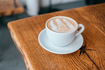 A cup of coffee with beautiful latte art in a white cup on rustic wooden table background.