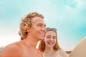 Surfers at the beach- Smiling couple of surfers walking on the beach and having fun in summer. Extreme sport and vacation concept