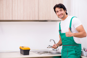 Young plumber repairing tap at kitchen  