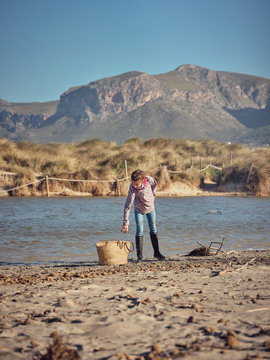 Girl near basket picking up garbage from river shore