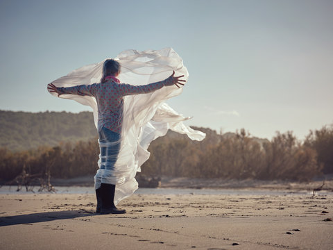Girl entangled in waving textile on river coast