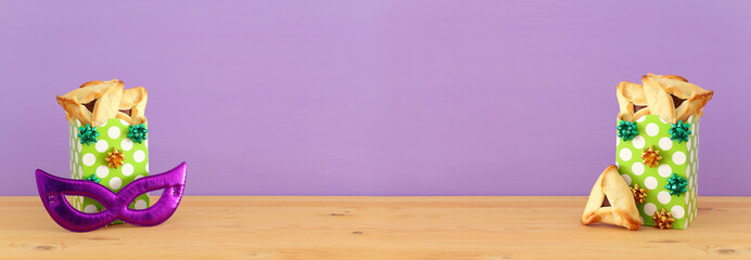 Purim celebration concept (jewish carnival holiday). Traditional hamantaschen cookies over wooden table and purple background.