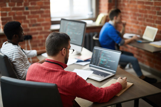 Group of contemporary it-engineers sitting b ydesks in front of computers and learning new software or codes