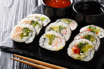 Futomaki rolls with various fillings are served with sauces close-up on a slate board. horizontal