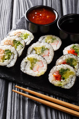 Freshly made rolls with various fillings served with soy and chili sauces close-up on a slate board. vertical