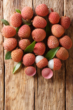 Ripe lychee fruits with green leaves close-up on wooden. Vertical top view